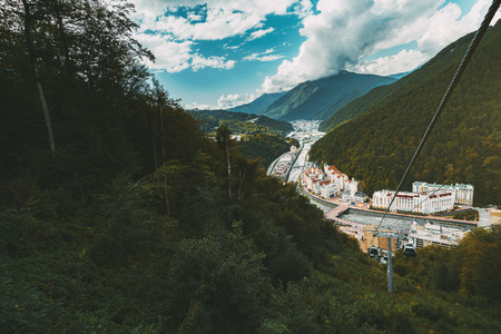 Wide-angle shooting from funicular cabin of autumn mountain scenery with small settlement Estosadok in valley, filled with multiple resort buildings; ropeway on the right, sunny day, Sochi, Russiaの写真素材