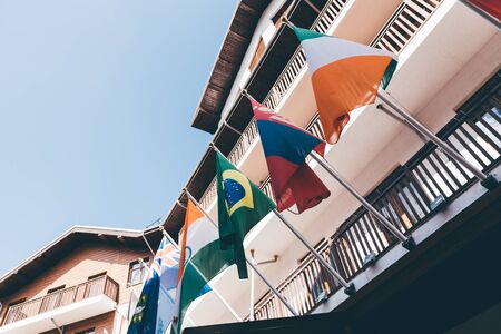 Multiple colorful national flags of different countries fixed to wooden facade of houses on sunny...