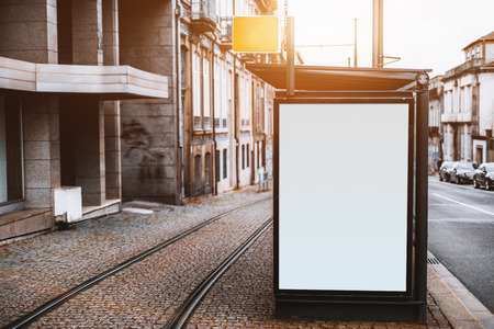 Close-up view of empty white informational banner mockup in urban settings between road and tramway; blank billboard placeholder template outdoors on city tram stop, pavement stone, sunny dayの写真素材