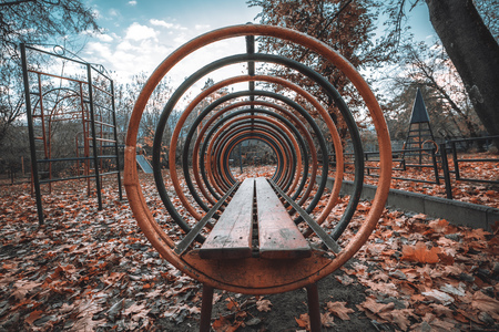 Wide-angle view of playground heap up with dry orange autumn leaves on the ground, with metallic construction consisting of equidistant iron hoops of different color following into vanishing pointの写真素材