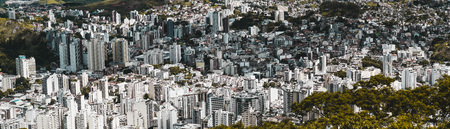 Panoramic shot of an urban landscape from high above of Juiz de Fora town in Minas Gerais state of Brazil: multiple multistorey residential and office buildings, favelas, parks, and hills, bright dayの写真素材