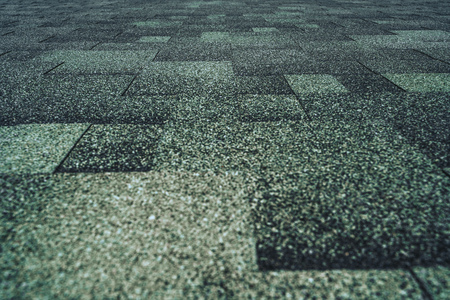 Soft roof tiled greenish grainy texture on the top of a summer house lit by the sun; green soft roofing tiles covering a building, focus on the middle distanceの写真素材