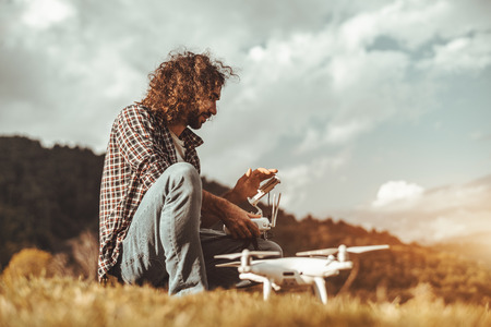 Side view of a curly Caucasian man with the beard using the screen of the gadget to launch his drone...