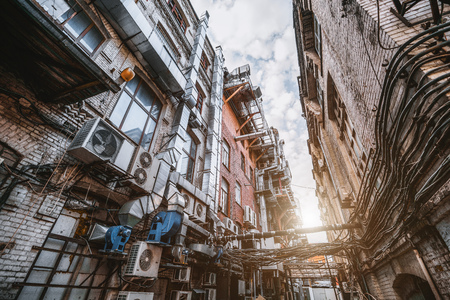 Narrow atmospheric backstreet between two houses with a huge number of wires stretching into the distance and outdoor air conditioning units, and plenty of ventilation tubes on the brick wallsの写真素材