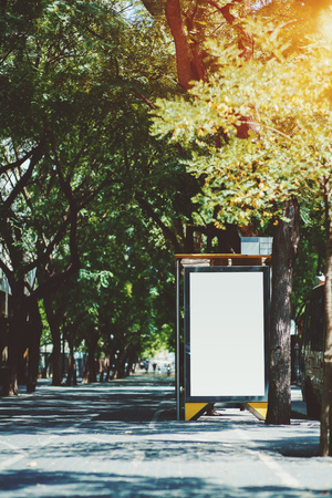 The billboard placeholder template outside of city bus stop, the sidewalk on the left; vertical blank advertising banner mock-up in urban settings; white empty informational signboard on the streetの写真素材