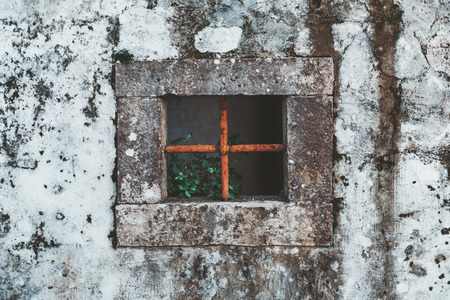The fragment of an old grungy antique wall in Sintra, Portugal with a square stone window hole in...