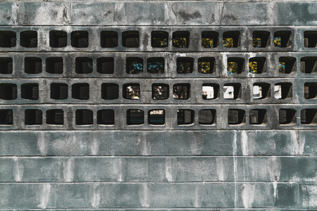 The frontal texture of an outdoor grungy contemporary wall with traces of white leaks and with a section of bricks laid across with transparent holes through which the backyard is visibleの写真素材