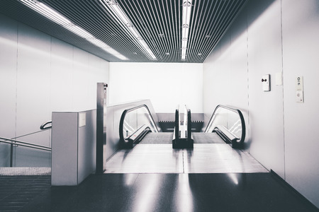 A contemporary doubled escalator and stairway in an airport terminal or railway station depot or a modern shopping mall, an emergency stop button and intercom on the wall, soundproof striped ceilingの写真素材