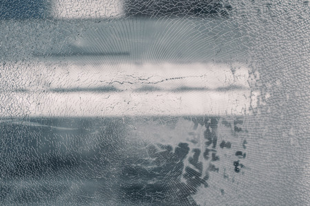 The texture of broken glass; close-up view of a broken windshield with a blurry background behind...