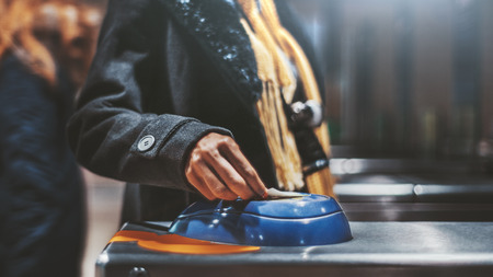 Close-up view of a hand of a female tourist putting a ticket onto a blue magnet electronic area of a chromed turnstile in the subway or a railway station depot, selective focus, shallow depth of fieldの写真素材