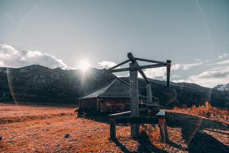 An autumn wide-angle landscape in Altai mountains with a ridge overgrown with fall trees in the background and a glade in the foreground with an abandoned wooden shack and table to eatの写真素材