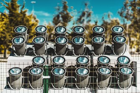Several fenced rows of powerful spotlights directed upwards on the ground as a part of landscape lighting equipment installation outdoors to illuminate big objects at night, with trees behindの写真素材