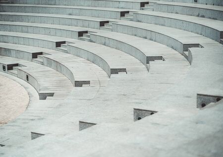 Rows of grayish stony or marble seats and flights of stairs of a modern outdoor amphitheater with a pavement stone on the stage down belowの写真素材