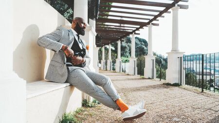 An old-fashioned bald bearded African man is putting his watch on a chain into his pocket while...