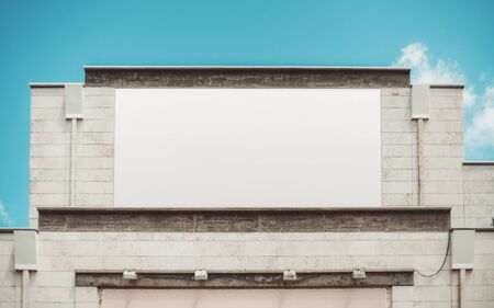 An empty huge poster mockup on the roof of a shopping mall or a cinema; a white template placeholder of an advert billboard on the rooftop of a building; blank mock-up of an outdoor information bannerの写真素材