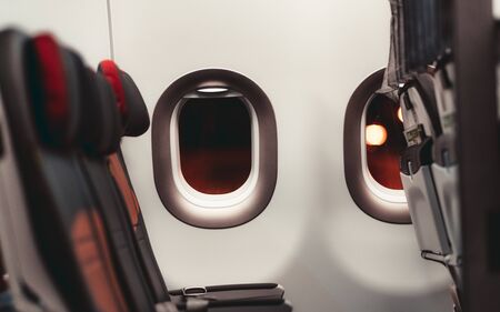 A dark aircraft interior: the row of modern empty leather seats with armrests down, shallow depth of field, selective focus on the the window with a night lights outsideの写真素材