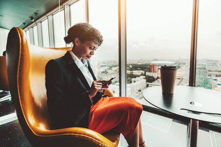 A young pensive African-American woman entrepreneur is reading a message on the screen of her...
