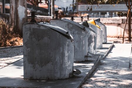 Five huge outdoor metal containers in a row for separate garbage collection standing on iron base in the tree shadow on the street, Sintra, Portugalの写真素材