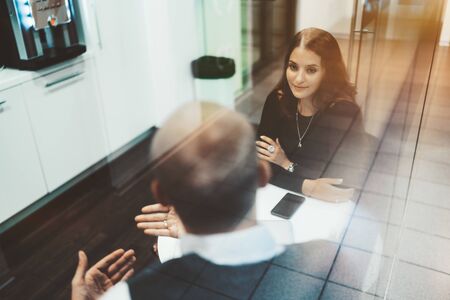A charming caucasian woman entrepreneur with a long hair is listening attentively her male colleague during a break while both sitting at the table of a modern office kitchen and talkingの写真素材