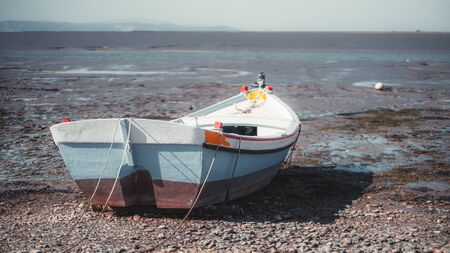 Rearview of an old colorful painted wooden rope-bound fishing boat on the pebble of the river bank with a horizon and waterscape behind in a defocused background, Alcochete, Portugalの写真素材