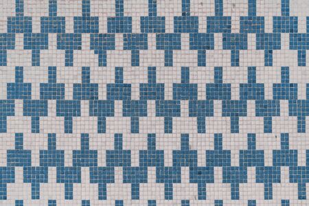 Front view of a tiled wall texture consisting of small stone mosaic tiles of white and blue color...