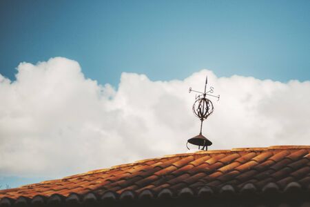 Minimalistic shot of an antique tiled roof of some residential house in Europe with an old rusty weather rickety vane on the top and a beautiful cloudscape in a defocused backgroundの写真素材
