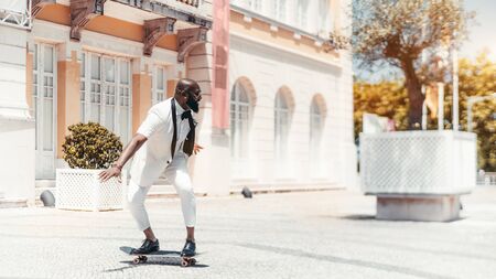 Laughing mature bald bearded African man is riding on a skateboard outdoors on a paving-stone on a sunny day, with a copy space area on the right for an ad text message or your logo, Sintra, Portugalの写真素材