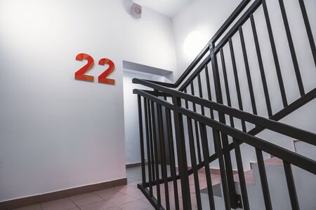 A typical flight of stairs in an office business skyscraper: clean white walls, metal fencing of the...