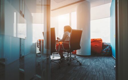 Rearview of African-American businesswoman on a meeting indoors of a boardroom of a luxury office; view from behind of a biracial woman entrepreneur sitting at the table in the meeting roomの写真素材