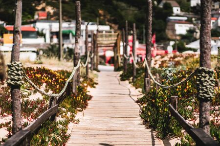 A long wooden outdoor passageway in a warm summer resort from the beach to the inner area: wooden fence, rope tied between pillars, shallow depth of field with a selective focus on the foregroundの写真素材
