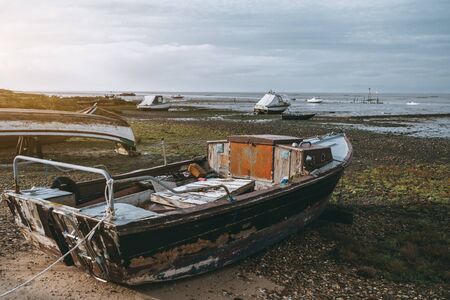 Old flaked fishing boat with a small cabin inside on the shallows on a forsaken pier in a wasteland;...