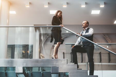 Two business partners having a conversation on the office stairs: a handsome man entrepreneur with a laptop in his hands and his female colleague -Â a caucasian businesswoman with the digital tabletの写真素材