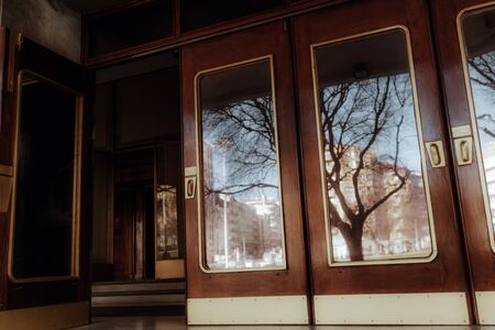 A row of beautiful wooden doors made in art nouveau style with brass fittings and mirror glasses reflecting a cityscape with bare trees and houses, one door is opened and there is a dark hall behindの写真素材