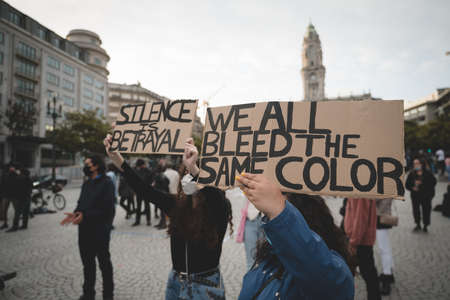 Porto, Portugal - June 6, 2020: demonstration against racial discrimination Black lives matter; two women in front of the crowd holding placards "silence is betrayal" and "we all bleed the same color"のeditorial素材