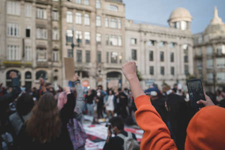 Porto, Portugal - June 6, 2020: the demonstration against racial discrimination Black lives matter; selective focus on a thrown up fist of a man, a crowd of protesting people in defocused backgroundのeditorial素材