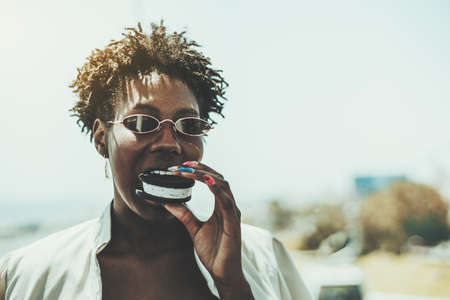 Close-up portrait of a dazzling young black woman in sunglasses and a white trench, with afro hair...