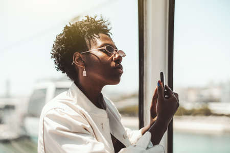 Portrait of an exquisite young fancy African woman tourist in a white trench and elegant sunglasses...