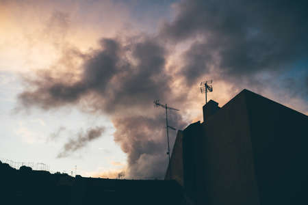 A deep evening wide-angle shot with a dark silhouette of a typical suburban residential house with old TV antennas on the top and a beautiful lilac skyscape in the background, dark keyの写真素材