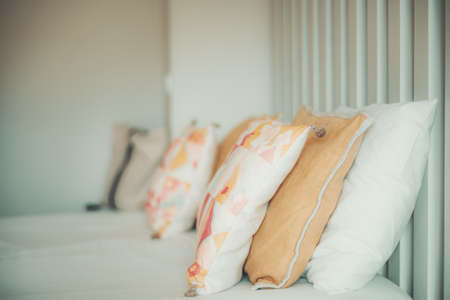 Side view of a bright neat made bed with rows of pillows and multicolored cushions on the top...