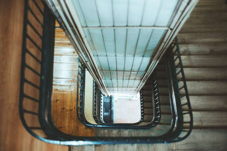 View from above with a shallow depth of field of a long stairwell going down in a spiral, an old residential building with a metal railing and a lift shaft in the center, selective focus in the middleの写真素材