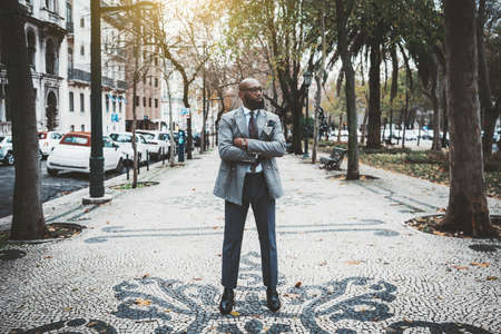 A stately mature hairless barbate black man entrepreneur in a dapper custom made suit is standing...