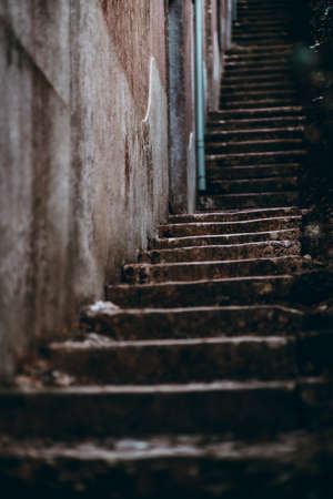 View of a long dark stone stair stretching up into the distance near a wall of an old building;...