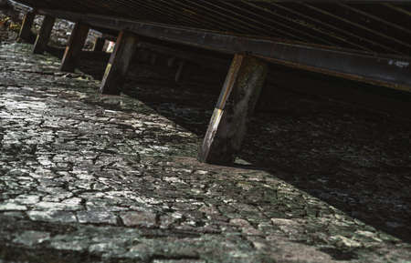 A mossy greenish stone textured surface under a pier at low tide covered with a crust of dried algae with metal pillars supporting the embankment and a contrast geometrical shadow under itの写真素材
