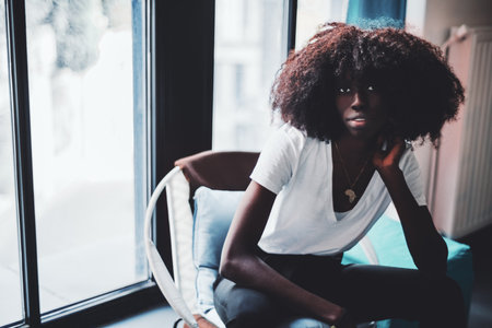 A portrait of a beautiful young African-American female with curly hair, in a white t-shirt and with...