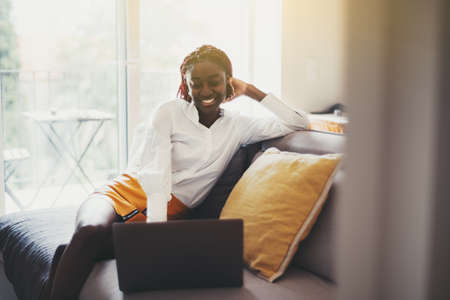 Portrait of a cheerful young black female sitting on the couch with cushions in a living room of her...