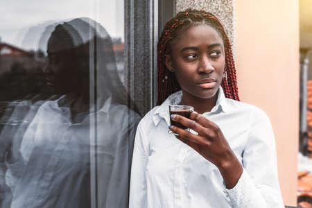 A portrait of a young dazzling black woman with red braids and in a white shirt, leaning against a...