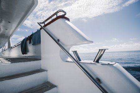 A fragment of a white safari diving boat with selective focus on chromium mooring bitts/bollards, wooden stairway leading to the deck of the vessel, and the railings; a warm sunny day, Maldivesの写真素材