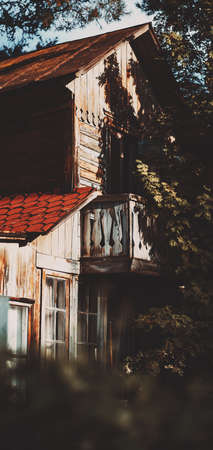 A perspective view of an old wooden house corner in the shadow of a rowan tree. Vertical view of a rustic cabin backyard on a sunny day. A wooden cottage with a selective focus on its old balconyの写真素材