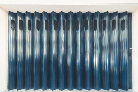 A garage or other entrance closed metal gate texture with white vertical fanfold lines of the door; front view of an accordion-folded blue door of big gates on the street, popular in Lisbon, Portugalの写真素材