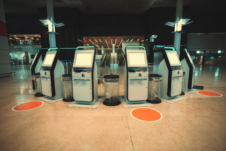 A curved set of self-serve flight check-in electronic kiosks in an airport with mockups of LCD screens; 6 electronic ticket terminals, templates of screens, social distancing stickers on the floorのeditorial素材